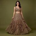 Model in a bronze brown net fish cut lehenga with sequinned ruffle tiers, a fitted 3D floral yoke and a sleeveless V-neck floral blouse against an olive backdrop