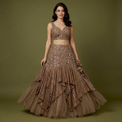 Model in a bronze brown net fish cut lehenga with sequinned ruffle tiers, a fitted 3D floral yoke and a sleeveless V-neck floral blouse against an olive backdrop