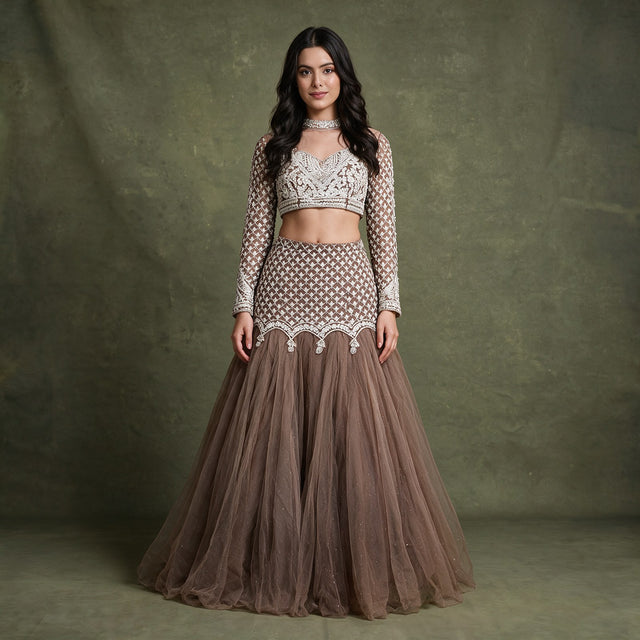 Model in a mocha brown net fish cut lehenga with an ivory beaded lattice yoke and a full-sleeve illusion-neck blouse against an olive backdrop