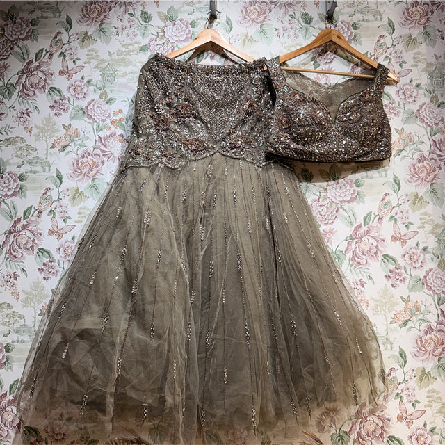 Olive taupe net fish cut lehenga and blouse on hangers against floral wallpaper, showing the beaded lattice yoke with 3D flowers and the net skirt