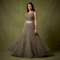 Model in an olive taupe net fish cut lehenga with a beaded diamond-lattice yoke, vertical bead lines and a sleeveless illusion-neck blouse against an olive backdrop