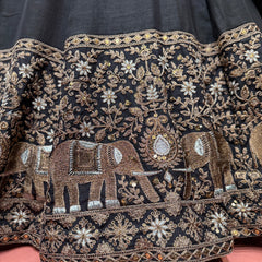 Black fabric close-up with embroidered elephant motifs, floral vines, gold-toned detailing