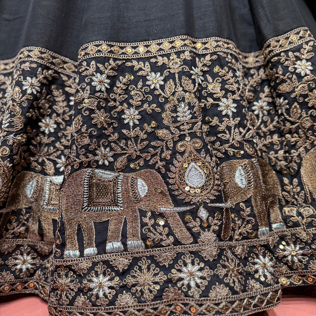 Black fabric close-up with embroidered elephant motifs, floral vines, gold-toned detailing