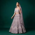 Model in a lavender net lehenga with silver sequin and stone chevron panels, V-neck blouse and lattice net dupatta against a green backdrop