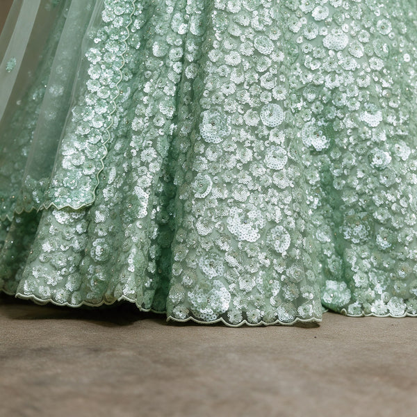 Close-up of pista green net lehenga hem with dense sequin florets and scalloped edge