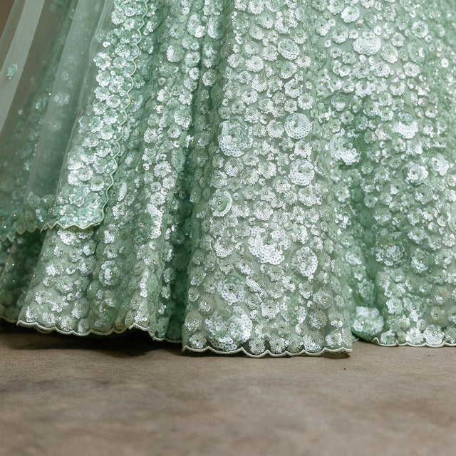 Close-up of pista green net lehenga hem with dense sequin florets and scalloped edge