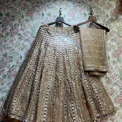 Ivory gold net lehenga and net dupatta on hangers against floral wallpaper, showing the vertical mirror columns and mirror-edged hem