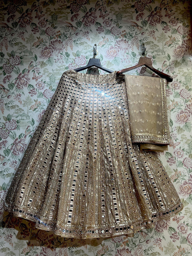 Ivory gold net lehenga and net dupatta on hangers against floral wallpaper, showing the vertical mirror columns and mirror-edged hem
