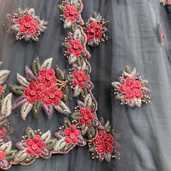 Embroidered floral motifs on dove-gray fabric with red-pink blooms and leaf accents