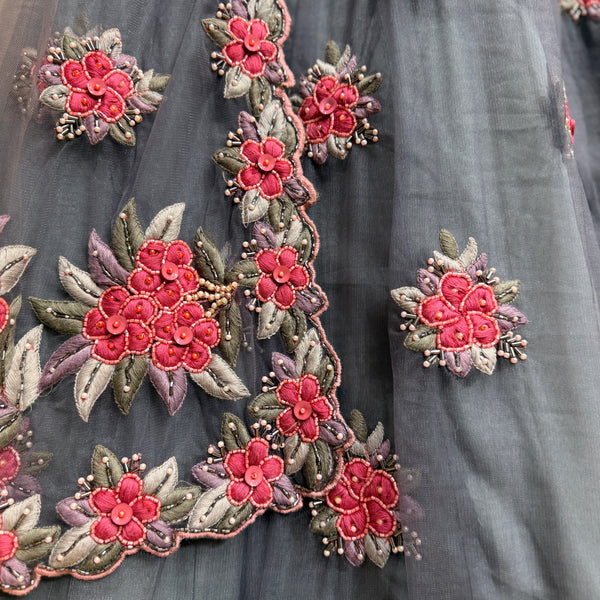 Embroidered floral motifs on dove-gray fabric with red-pink blooms and leaf accents