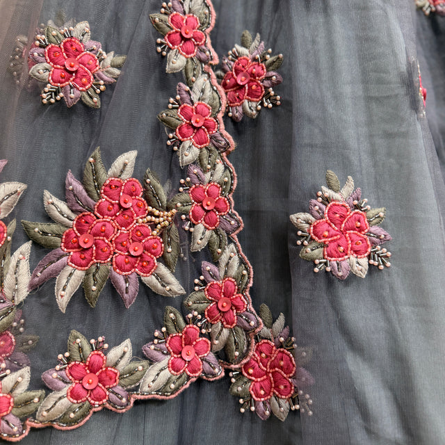 Close-up of pink and green floral hand embroidery on grey fabric