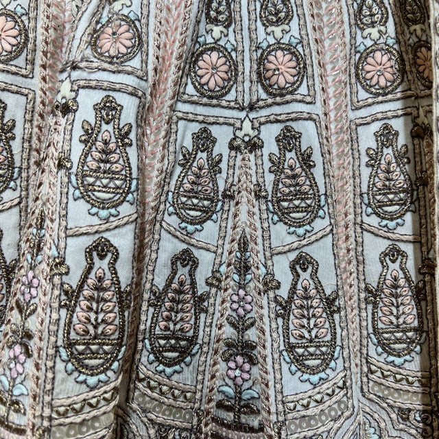 Off-white lehenga fabric close-up with vertical patchwork embroidery and paisley motifs