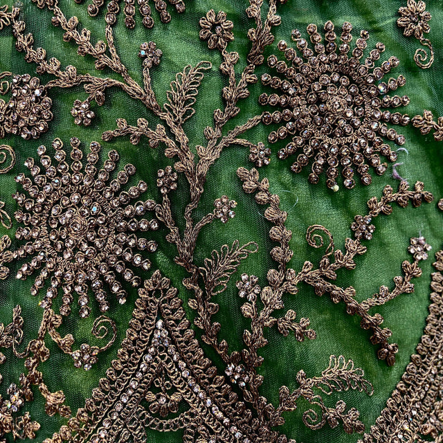 Green lehenga fabric close-up with dense gold-toned sequin and thread embroidery.