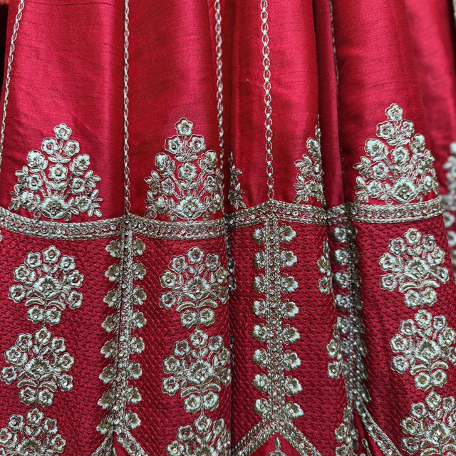Red lehenga fabric close-up with ornate silver floral embroidery and chain motifs