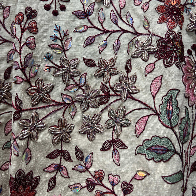 Close-up floral embroidery on ivory fabric with pink, maroon, and teal accents