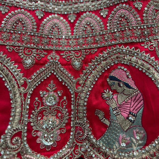 Close-up of red lehenga fabric with ornate silver, teal and beadwork border