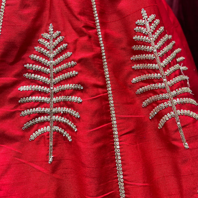 Close-up of red lehenga fabric with silver-gold bead embroidery and tree-like motif panels
