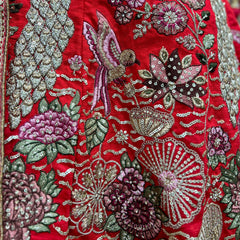 Red embroidered bridal lehenga fabric with floral motifs, birds, and silver zari accents