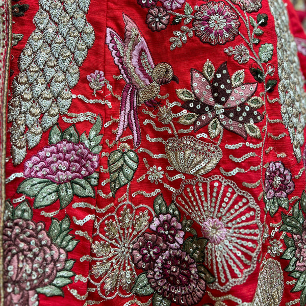 Red embroidered bridal lehenga fabric with floral motifs, birds, and silver zari accents