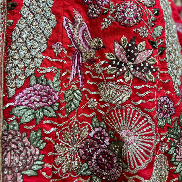 Red embroidered bridal lehenga fabric with floral motifs, birds, and silver zari accents