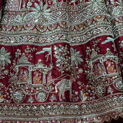 Maroon lehenga fabric close-up with embellished floral and figure motifs, silver trim