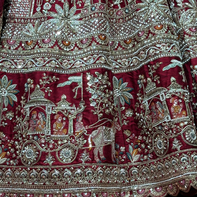 Maroon lehenga fabric close-up with embellished floral and figure motifs, silver trim