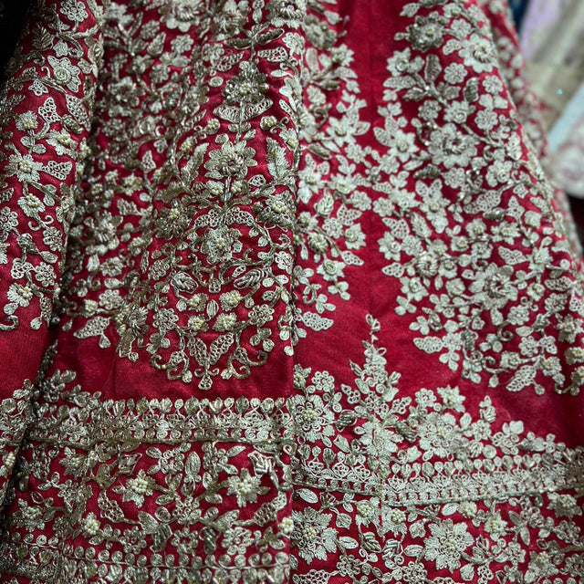 Red raw silk lehenga fabric close-up with dense silver-gold floral embroidery and border