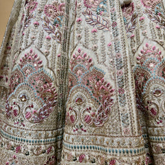 Ivory lehenga fabric close-up with detailed floral paisley embroidery in pink and teal.