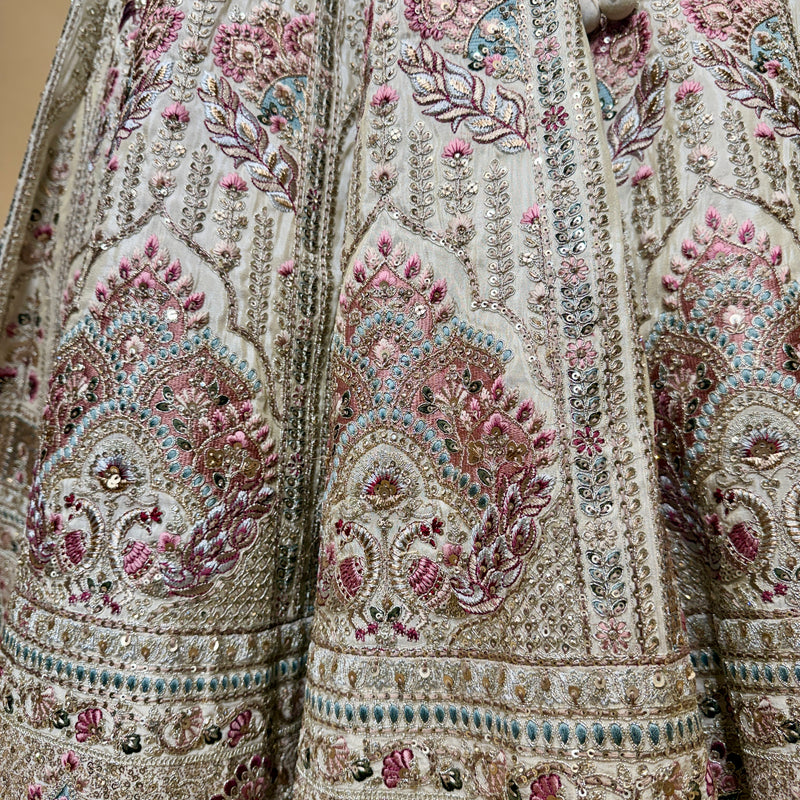 Ivory lehenga fabric close-up with detailed floral paisley embroidery in pink and teal.