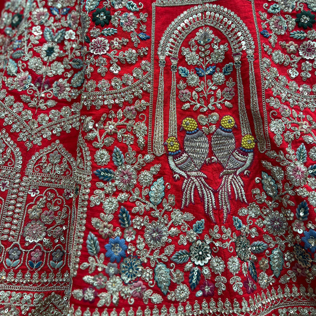 Red embroidered bridal dress fabric with teal, floral motifs and beaded deity panel