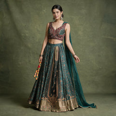 Model in a teal viscose lehenga with a gold hem border, a wine handwork blouse and a teal chinon dupatta, holding dandiya sticks