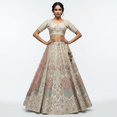 Model in an ivory raw silk lehenga with pink, mint and gold embroidered teardrop and diamond motifs, a lattice-sleeved blouse and a pink net dupatta, against a white backdrop