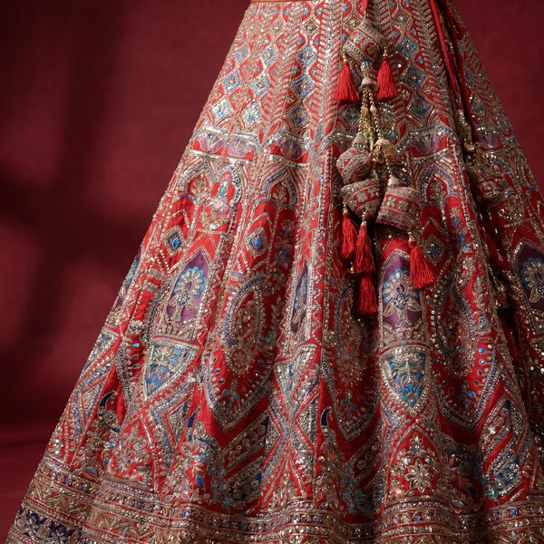 Red bridal lehenga skirt in raw silk with ornate multicolor embroidery and tassel trim