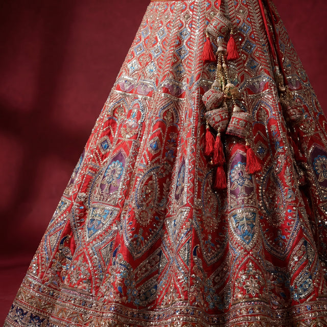 Red bridal lehenga skirt in raw silk with ornate multicolor embroidery and tassel trim