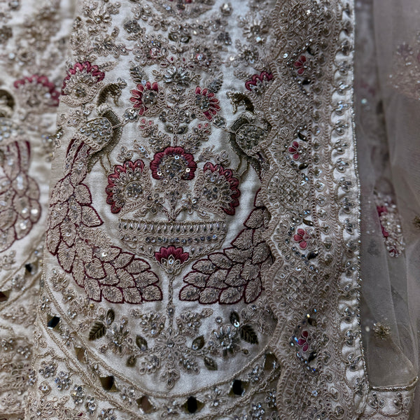 Embellished ivory fabric panel with mirror details and red-green zari embroidery close-up