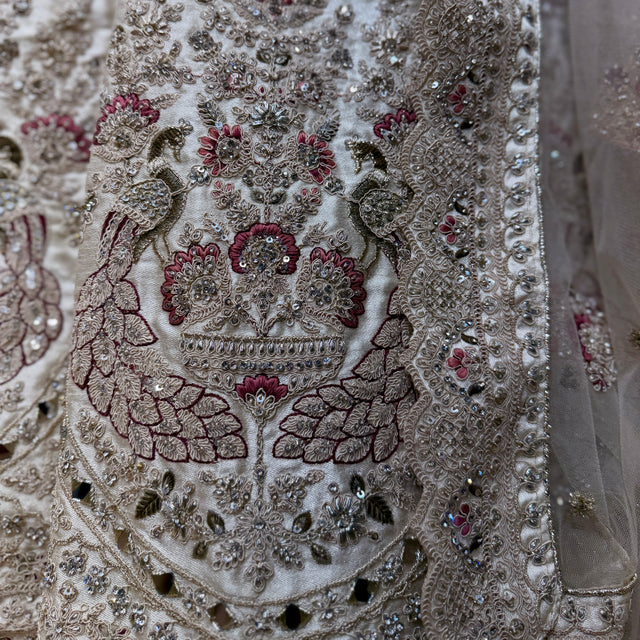 Embellished ivory fabric panel with mirror details and red-green zari embroidery close-up