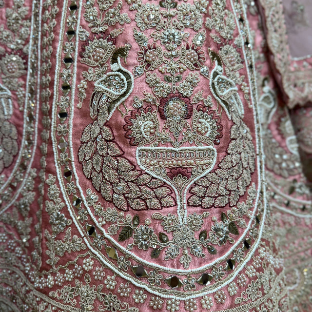Close-up of soft pink lehenga embroidery with gold-tone and green beaded motifs