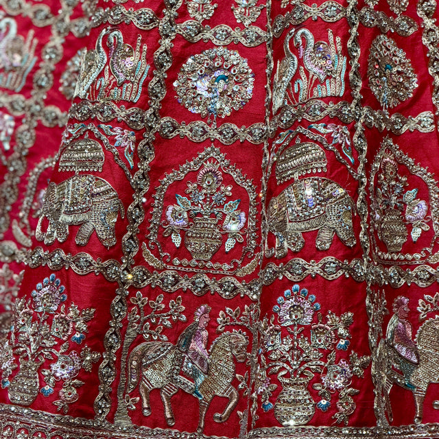 Red silk lehenga fabric close-up with silver embroidery motifs and jeweled detailing