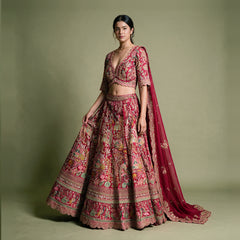 Model in a pink raw silk bridal lehenga with village-scene meenakari resham embroidery, scalloped V-neck blouse and organza dupatta against an olive backdrop