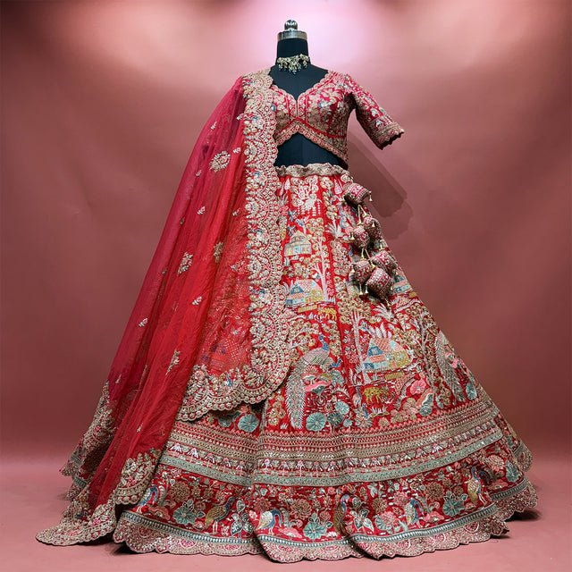 Red raw silk lehenga set on a mannequin with heavy organza cutwork dupatta, tassels and village-scene embroidery