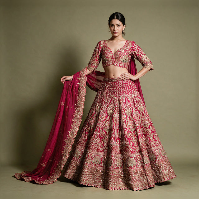 Model in a pink and gold zari and stone work lehenga with a V-neck blouse and heavy organza dupatta against an olive backdrop