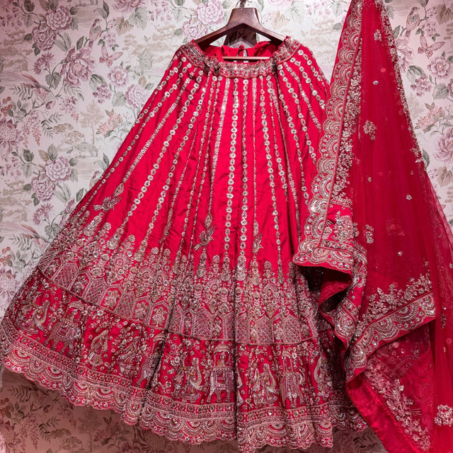 Rani pink raw silk lehenga with elephant procession hem and embroidered net dupatta on hanger
