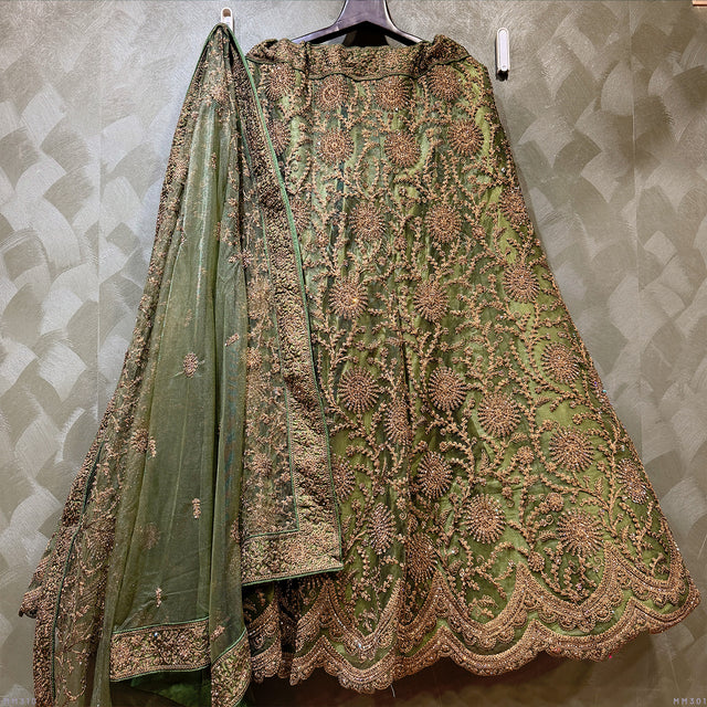 Green lehenga with ornate gold zari embroidery and matching sheer dupatta on hanger.