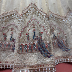 Close-up of ivory lehenga embroidery with blue peacock motif, beads, and decorative borders