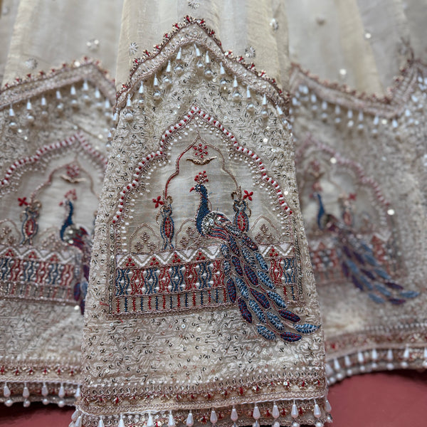 Close-up of ivory lehenga embroidery with blue peacock motif, beads, and decorative borders