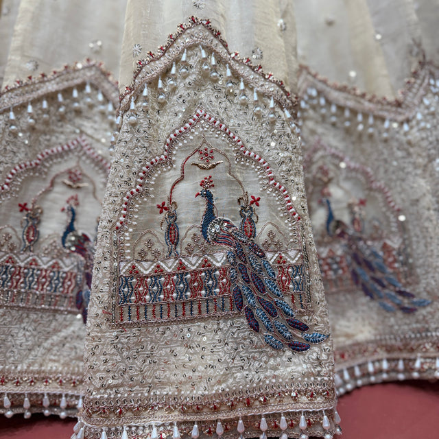 Close-up of ivory lehenga embroidery with blue peacock motif, beads, and decorative borders