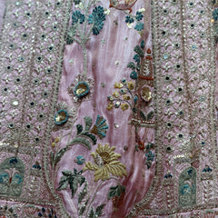 Close-up of blush lehenga fabric with dense teal-and-gold floral and bird embroidery