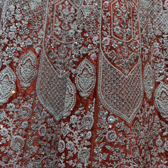 Close-up of paisley embroidery on lehenga fabric in teal, red, and silver-toned threadwork