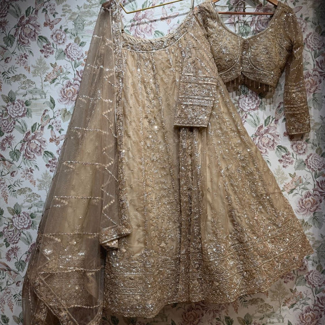 Gold net lehenga set laid flat: skirt, stitched blouse with beaded fringe and dupatta