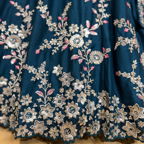 Close-up of blue lehenga fabric with silver floral embroidery and tiny pink accents